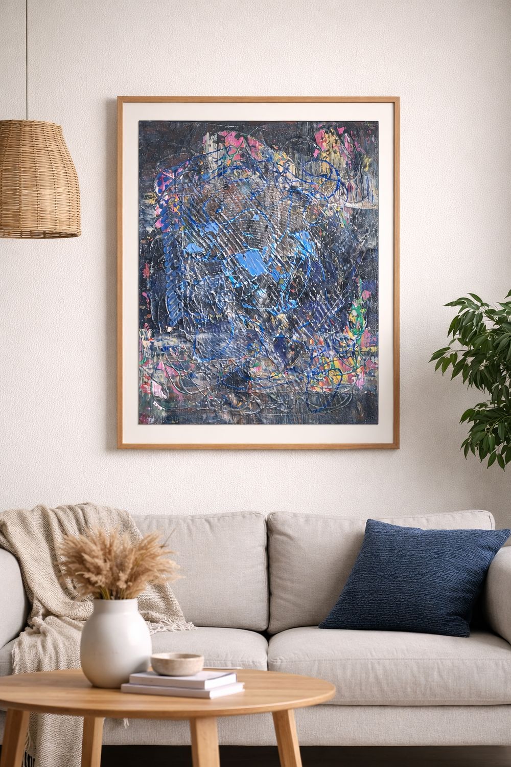 A framed work on paper above a pale sofa